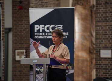 Essex Chambers of Commerce Chief Executive Denise Rossiter addresses the conference. She is standing at a lectern, making a speech. The PFCC logo is in the background of the photo.